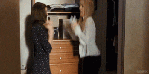 Two Women Are Standing Next To Each Other In Front Of A Dresser In A Room . GIF