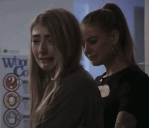 Two Women Are Standing Next To Each Other In Front Of A Sign That Says Who GIF