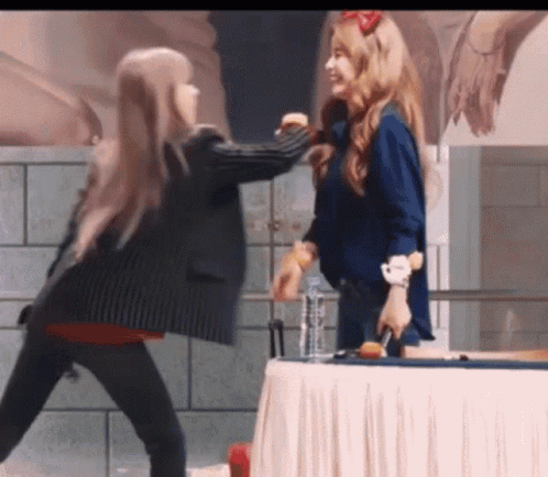 Two Women Are Standing Next To Each Other In Front Of A Table GIF