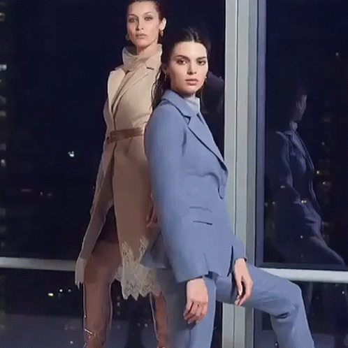Two Women Are Standing Next To Each Other In Front Of A Window . One Of The Women Is Wearing A Blue Suit . GIF
