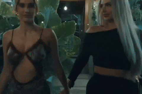 Two Women Are Standing Next To Each Other In Front Of Plants GIF