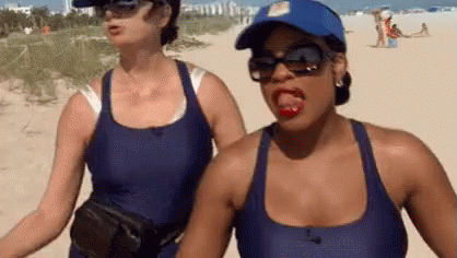 Two Women Are Standing Next To Each Other On A Beach And One Of Them Is Sticking Out Her Tongue . GIF