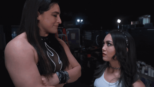 Two Women Are Standing Next To Each Other With Their Arms Crossed And One Has A Choker Around Her Neck GIF