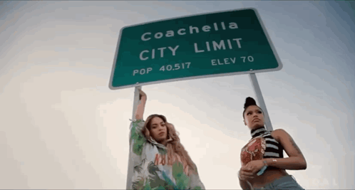 Two Women Are Standing Under A Sign That Says Coachella City Limit GIF