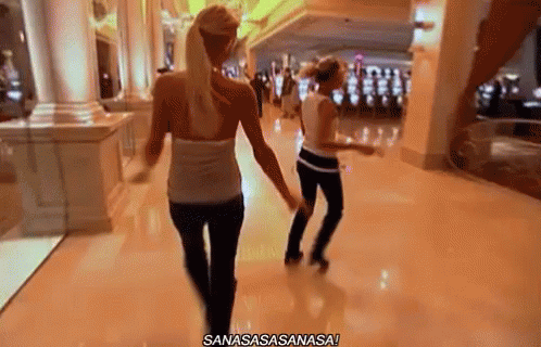 Two Women Are Walking Down A Hallway In A Casino And One Of Them Is Dancing . GIF