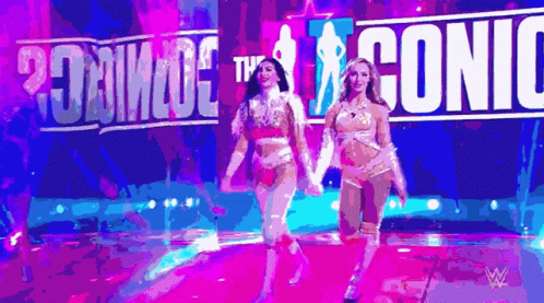 two women are walking on a stage in front of a sign that says ' iconic '
