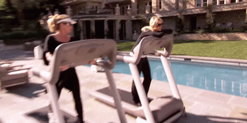 Two Women Are Walking On Treadmills In Front Of A Pool . GIF