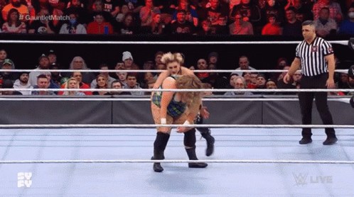 Two Women Are Wrestling In A Ring While A Referee Watches . GIF