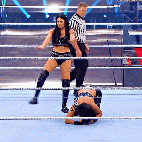 Two Women Are Wrestling In A Ring With A Referee Standing Behind Them GIF