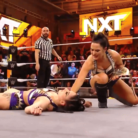 Two Women Are Wrestling In A Ring With A Sign That Says Nxt On It GIF