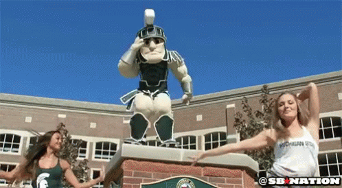 Two Women Dancing in Front of Spartan Warrior Statue