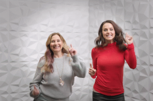 Two Women Dancing in Front of White Wall One in Red Shirt