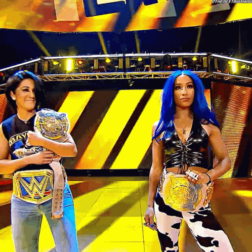 Two Women Holding Wrestling Belts on Stage