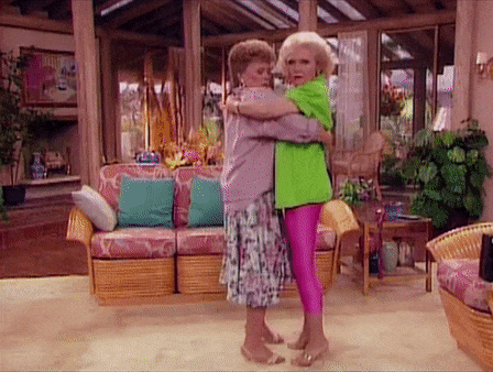 Two Women Hugging In A Living Room With A Couch And Chairs GIF