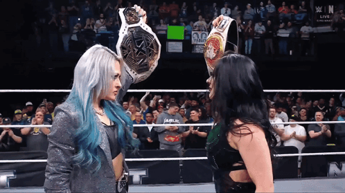 Two Women In A Wrestling Ring With One Holding A Belt That Says Champion GIF