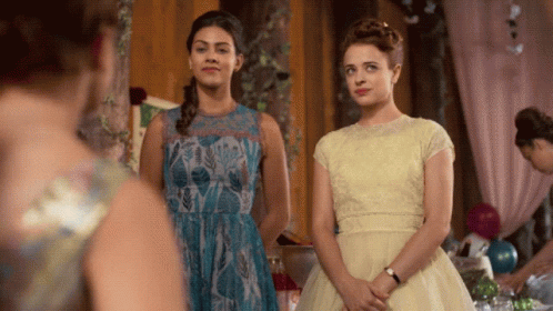 Two Women In Dresses Are Standing Next To Each Other In A Room GIF