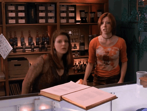Two Women in Front of Shelf With Bottles and Sign Saying A