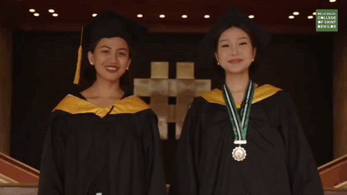 Two Women In Graduation Gowns Next To Palawulang Sign GIF
