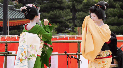 Two Women In Kimonos Are Dancing In Front Of A Red And White Curtain GIF