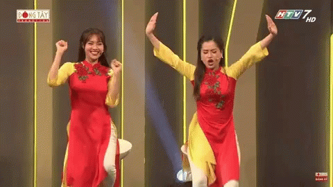 Two Women in Red and Yellow Dresses on Stage With Arms Up