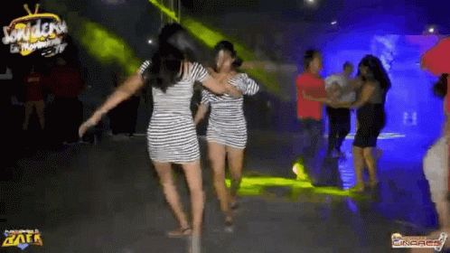 two women in striped dresses are dancing on a dance floor in a club .