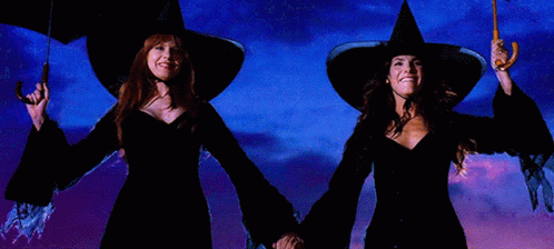 two women in witch hats holding umbrellas in front of a blue sky