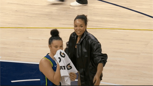 Two Women On A Basketball Court With One Holding A Shirt That Says Atg GIF