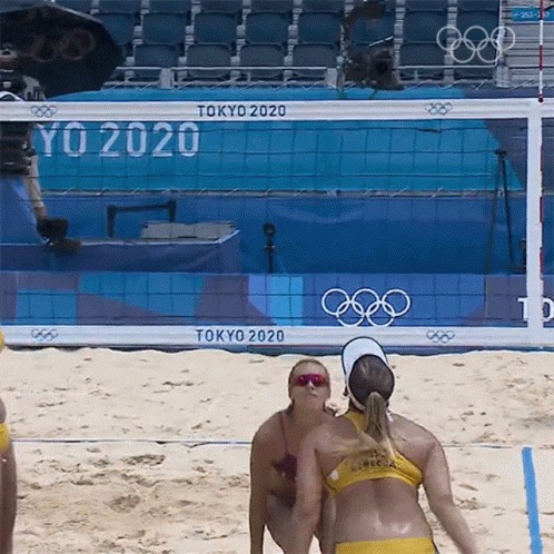 Two Women Playing Beach Volleyball In Front Of A Tokyo 2020 Sign GIF