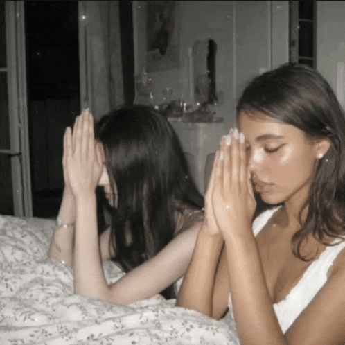 Two Women Praying With Their Hands Folded Over Their Faces GIF