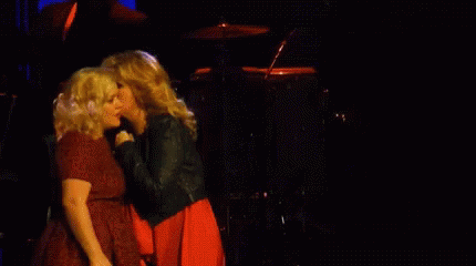 Two Women Singing In Front Of A Drum Set In A Dark Room GIF