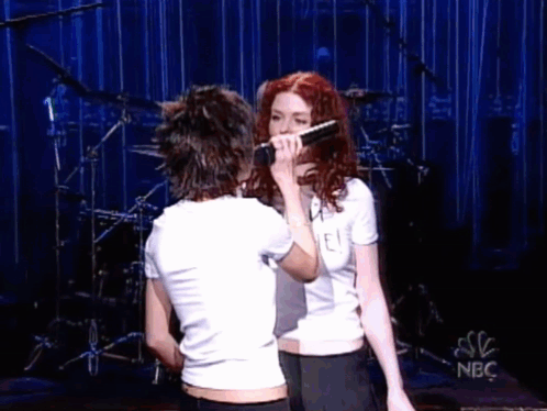 Two Women Singing Into Microphones On Stage GIF