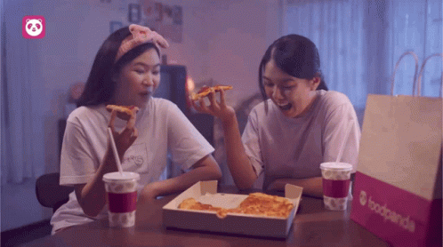 Two Women Sit At A Table With A Box Of Pizza And A Bag That Says Foodpanda GIF