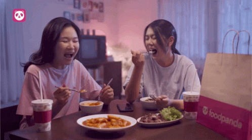 Two Women Sit At A Table With Food And A Bag That Says Foodpanda On It GIF