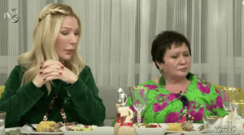Two Women Sit At A Table With Plates Of Food And A Sign That Says Seda Sayan Ile On It GIF