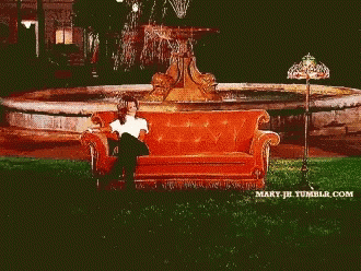 Two Women Sit On A Couch In Front Of A Fountain GIF