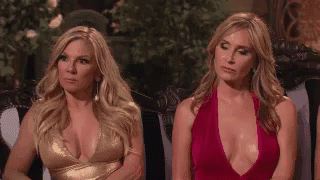 Two Women Sitting on Couch, One in Plunging Dress