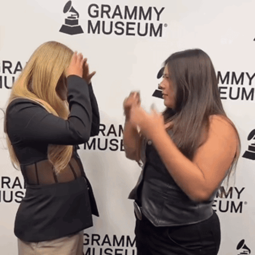 Two Women Standing In Front Of A Grammy Museum Sign GIF