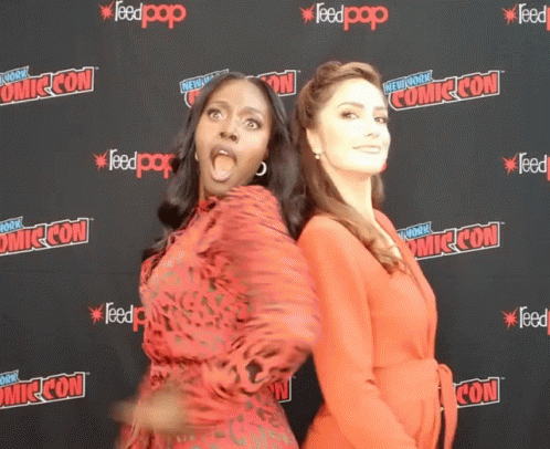 Two Women Standing In Front Of A Wall That Says Comic Con On It GIF