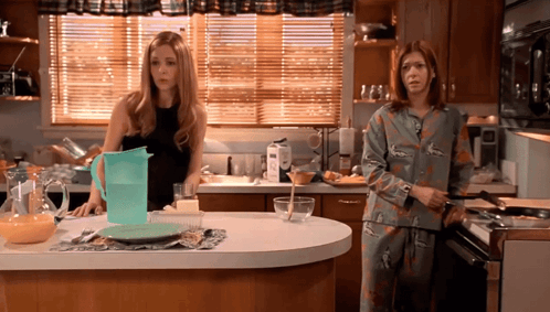 Two Women Standing in Kitchen With Pitcher of Water