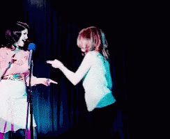 Two Women Standing Next To Each Other On A Stage GIF