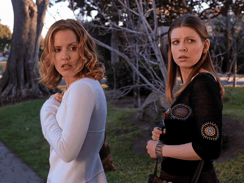 Two Women Standing Next To Each Other With One Wearing A Black Top GIF