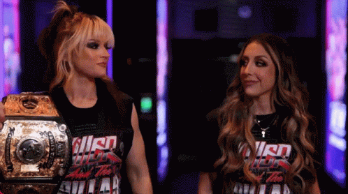 Two Women Standing Next To Each Other With One Wearing A T-Shirt That Says ' Smack Down ' On It GIF