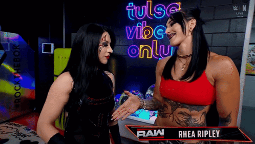 Two Women Talking In Front Of A Sign That Says Tulsa Vibe Only GIF