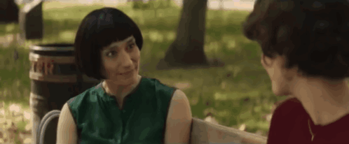 Two Women Talking on Park Bench, One With Wig