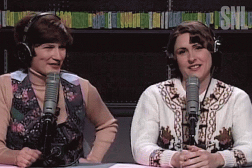 two women wearing headphones are sitting in front of microphones and the word snl is on the shelf behind them