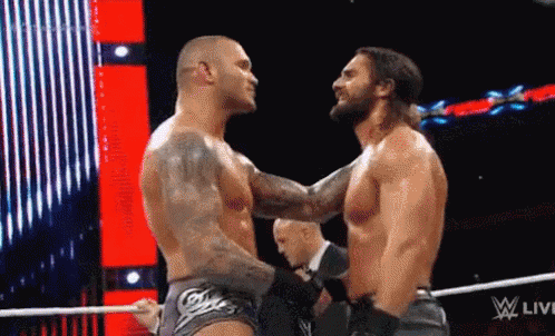 Two Wrestlers Are Hugging Each Other In A Wrestling Ring While A Referee Watches . GIF
