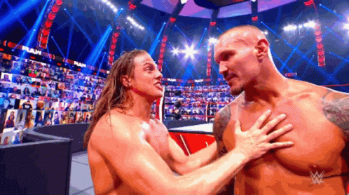 Two Wrestlers Are Hugging Each Other In A Wrestling Ring With A Crowd In The Background . GIF