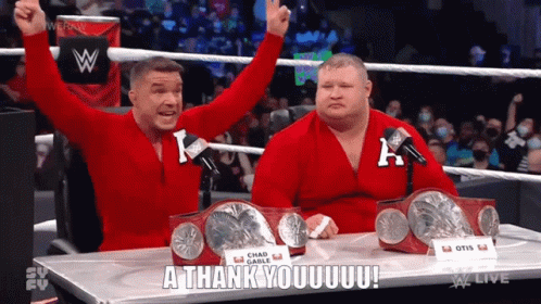 Two Wrestlers Are Sitting At A Table With Their Arms In The Air And One Of Them Is Saying A Thank You GIF