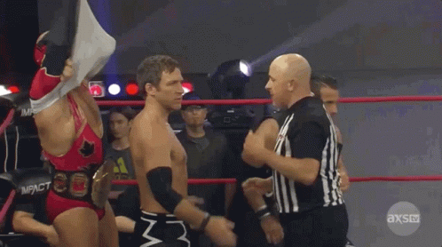 Two Wrestlers Are Standing In A Ring With A Referee In Front Of Them And The Referee Is Wearing An Axs Uniform GIF