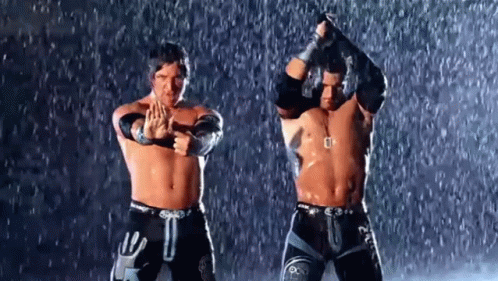 Two Wrestlers Are Standing In The Rain With Their Arms In The Air . GIF